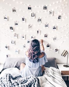 a woman sitting on top of a bed in front of a wall with pictures and string lights