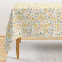 a table covered with a yellow and blue flowered cloth on top of a white rug