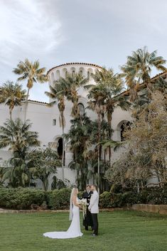 a bride and groom standing in front of a building with palm trees on the lawn