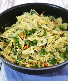 a bowl filled with pasta and vegetables on top of a blue cloth next to a wooden table