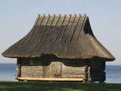 an old log cabin with a thatched roof near the ocean and grass on the ground