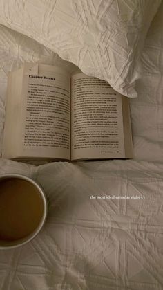 an open book sitting on top of a white bed next to a cup of coffee