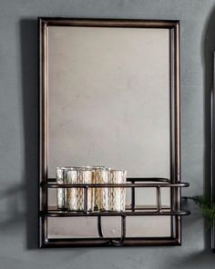 a mirror and some cups on a shelf in front of a wall mounted candle holder