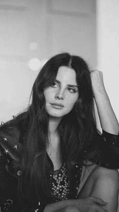 black and white photograph of a woman with long hair in leather jacket leaning on wall