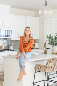 a woman sitting on top of a kitchen counter next to a bar with stools