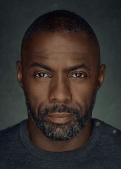 a close up of a person with a beard and blue shirt in front of a dark background