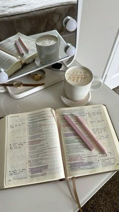 an open book sitting on top of a white table next to a cup and pen