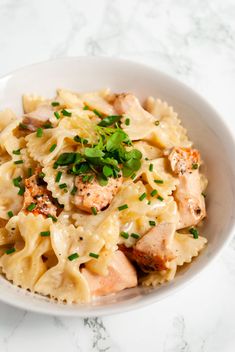 a white bowl filled with pasta covered in chicken and parsley on top of a marble table