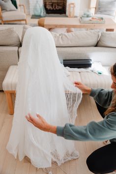 a woman kneeling on the floor next to a white wedding dress in front of a couch