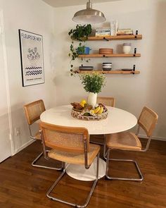 a white table with four chairs and a bowl of fruit on top of it in a room