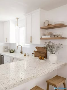 a kitchen with white cabinets and marble counter tops, wooden stools and open shelving