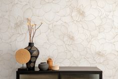 a table with vases and other items on it in front of a floral wallpaper