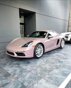 a pink porsche sports car parked in front of a building with two other cars behind it