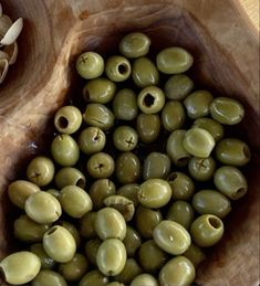 some green olives are in a wooden bowl