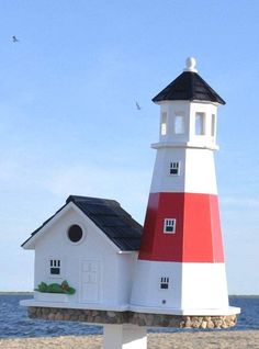 a white and red lighthouse shaped birdhouse on the beach