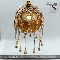 a golden ornament with beads and chains hanging from it's side on a ruler