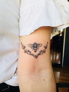 a bee tattoo on the back of a man's left arm, with vines and leaves around it