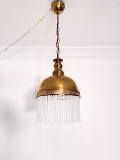 a light hanging from the ceiling in a room with white walls and a gold colored fixture