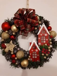 a christmas wreath hanging on the wall with ornaments around it and a house shaped ornament