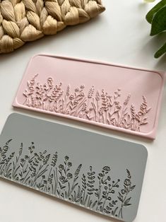 two metal trays with flowers on them sitting next to each other, one pink and the other gray