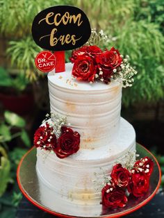 a white cake with red flowers and a sign that says ecom bakes on it