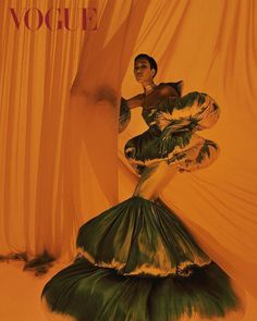 a woman in a green dress standing next to a curtain with the word vogue written on it