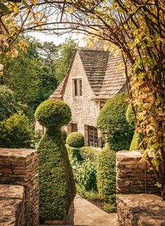 a stone house surrounded by trees and bushes in front of it is an archway that leads into the yard