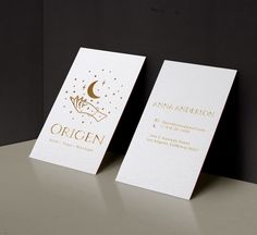 two white business cards with gold foil on them sitting next to each other in front of a black wall