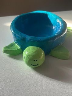 a plastic turtle toy sitting next to a blue bowl on top of a white table