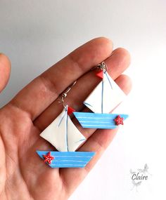 a hand holding two small white and blue sailboats with red stars hanging from it's sides