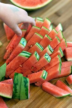 watermelon cut into pieces on a cutting board with text overlay that reads cut a watermelon for little fingers