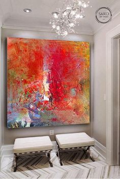 an abstract painting hangs on the wall above two stools in front of a chandelier