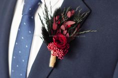 a boutonniere with red flowers and greenery on the lapel of a man in a blue suit