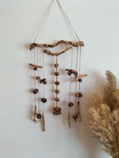 a wind chime hanging on the wall next to some dried flowers and branches in front of a white wall