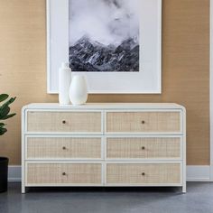 a white dresser with two vases sitting on top of it next to a painting