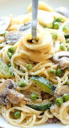 a plate of pasta with mushrooms, peas and asparagus is being eaten by a fork