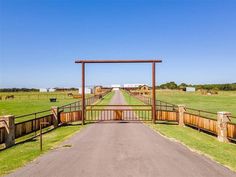 an open gate leading to a farm with cows grazing in the distance and green grass on either side