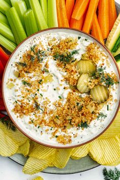 a bowl of dip surrounded by vegetables and crackers on a platter with carrots, celery, cucumbers