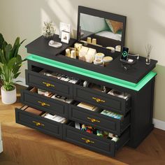 a black dresser with drawers and a mirror on the top, next to a potted plant