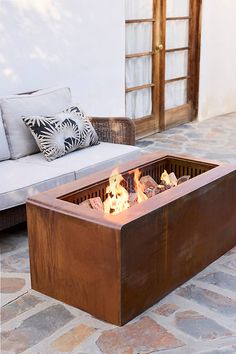 a fire pit sitting on top of a stone floor next to a couch and pillows