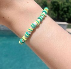 a woman's arm with a bracelet made out of glass beads and green, yellow and white stripes