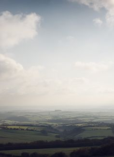 the view from an airplane looking down on green fields and rolling hills in the distance