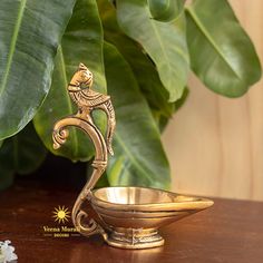 an ornate brass bowl on a table next to a large green leafy plant in the background