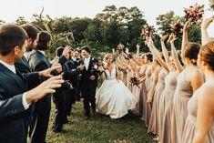 a group of people standing around each other on top of a grass covered field with their hands in the air