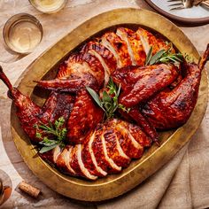 a platter filled with sliced turkeys and garnished with fresh herbs next to wine glasses