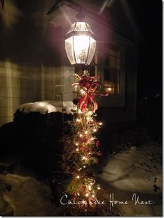 a lamp post decorated with christmas lights in front of a house on a snowy night