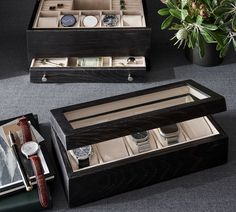 two wooden boxes with watch and watches inside on a table next to a potted plant