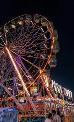 the ferris wheel is lit up at night in an amusement park with people standing around it