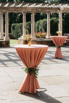 an outdoor setting with tables and chairs covered in orange draping, surrounded by greenery