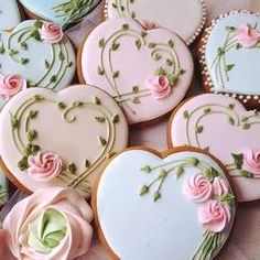 several decorated heart shaped cookies sitting on top of a table with pink roses and green leaves